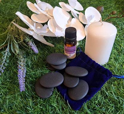 Product image with spa stones, lavender essential oil, candle, purple velvet bag, white orchid, and lavender flowers on green grass.
