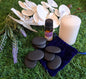 Product image with spa stones, lavender essential oil, candle, purple velvet bag, white orchid, and lavender flowers on green grass.